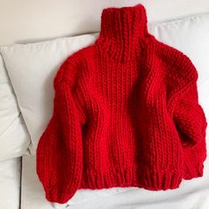 a red sweater sitting on top of a white pillow