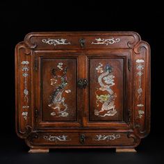 an ornate wooden cabinet with dragon carvings on it's doors and drawers, against a black background