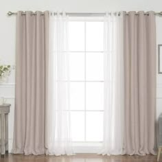 a living room with white walls and wooden flooring, two windows covered in sheer curtains