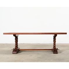 a large wooden table with two legs and a long slab on one end, in front of a white wall