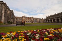 an old building with flowers in the foreground and a bench on the other side