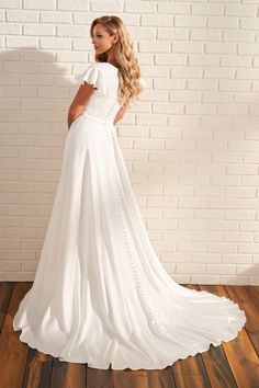 a woman standing in front of a brick wall wearing a white wedding dress with short sleeves