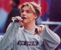 a young man holding a microphone in his right hand and singing into the microphone while standing next to an audience