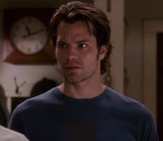 a man in a blue shirt standing next to a clock