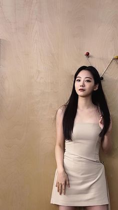 a woman with long black hair standing in front of a wall wearing a white dress