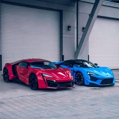 two blue and red sports cars parked next to each other in front of garage doors