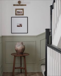 a vase sitting on top of a wooden table next to a stair case in a room