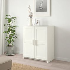 a white cabinet sitting next to a plant in a living room