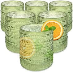 six green glass cups with oranges and mint leaves on the top one is filled with ice