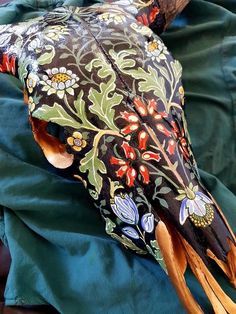 an animal skull is decorated with flowers and leaves on it's back end, resting on a green cloth