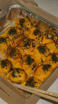 a box filled with chicken covered in cheese and broccoli next to chopsticks