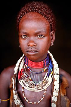 an african woman with large necklaces on her neck and headdress, looking at the camera