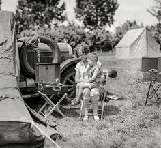 two young children sitting in chairs next to an old fashioned truck and campfirer