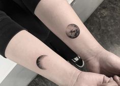 two people with matching tattoos on their arms holding each other's hands and looking at the moon