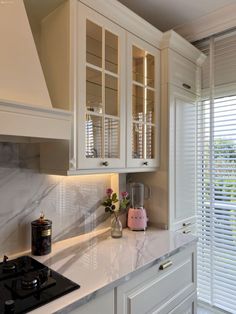 a kitchen with white cabinetry and marble counter tops, along with a pink vase filled with flowers