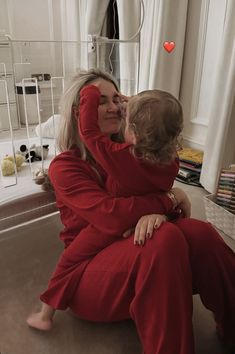 a woman sitting on the floor holding a child in her lap and kissing her cheek