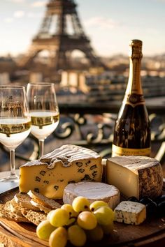 two glasses of wine, cheese and grapes on a table in front of the eiffel tower