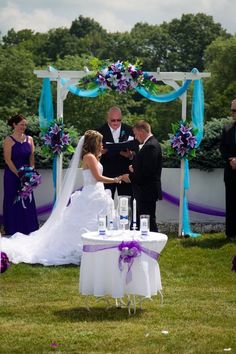 a bride and groom are getting married under an arch decorated with purple flowers at the end of their wedding ceremony