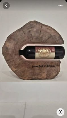 a bottle of wine sitting on top of a piece of wood in front of a white wall