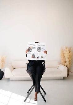 a woman sitting in a chair reading a paper on top of her face while looking at the camera