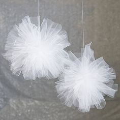 two white tulle balls hanging from strings on a gray background with silver sequins