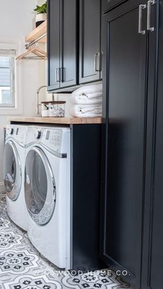 a washer and dryer in a laundry room with black cabinets, patterned floor tiles