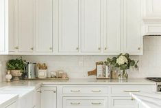 a kitchen with white cabinets and gold trimmings on the counter tops, along with flowers in vases