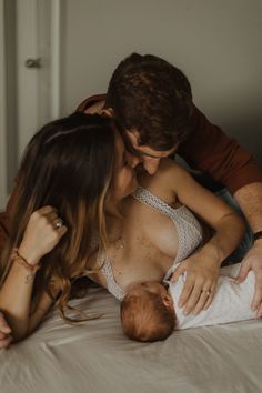 a man and woman cuddle their baby on the bed while she holds it up