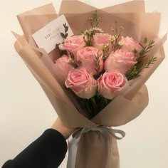 a bouquet of pink roses wrapped in brown paper with a note attached to the end