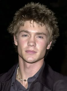 a close up of a person wearing a black jacket and necklace with hair in the wind