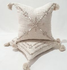 a white pillow with tassels on it sitting on a white floor next to a cushion