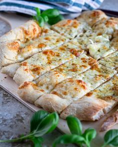 a pizza sitting on top of a wooden cutting board next to green leafy leaves