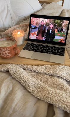 an open laptop computer sitting on top of a bed next to a cup and candle