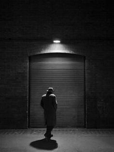 a man standing in front of a garage door at night with his back to the camera