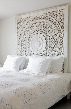 a bed with white sheets and pillows in a bedroom next to a wall hanging on the wall