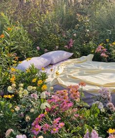 there is a bed in the middle of some flowers and plants with pillows on it