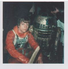 a man in an orange shirt next to a dalen star wars droid costume