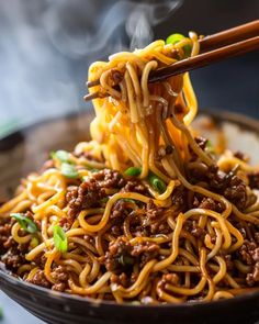 a bowl filled with noodles and meat being held by chopsticks over the top