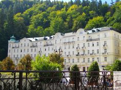 a large white building sitting on top of a lush green hillside next to a forest