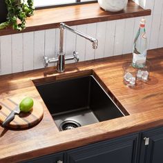 a kitchen sink sitting under a window next to a cutting board with an apple on it