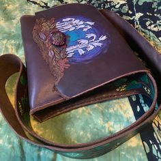 a brown leather purse sitting on top of a green and blue tablecloth covered bed