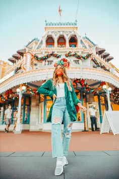 a woman standing in front of a building with christmas lights on the roof and decorations all around her