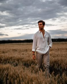 a man standing in the middle of a field with his hands in his pockets and looking at the camera