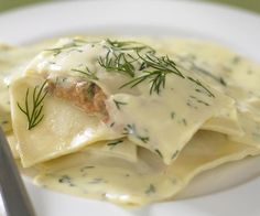 a white plate topped with ravioli covered in sauce and garnished with dill