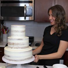 a woman standing in front of a white cake on top of a counter next to a microwave