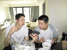 two young men sitting at a table looking at their cell phones