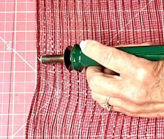 a person using a green handle on a red piece of cloth to cut fabric with scissors