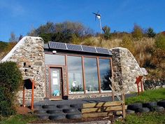 a small house made out of rocks with solar panels on the roof and windows in front