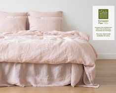 a bed with pink linens and pillows in a white room, next to a wooden floor