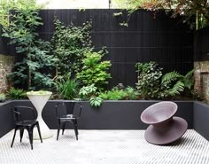 two black chairs and one white chair are in the middle of a courtyard with plants